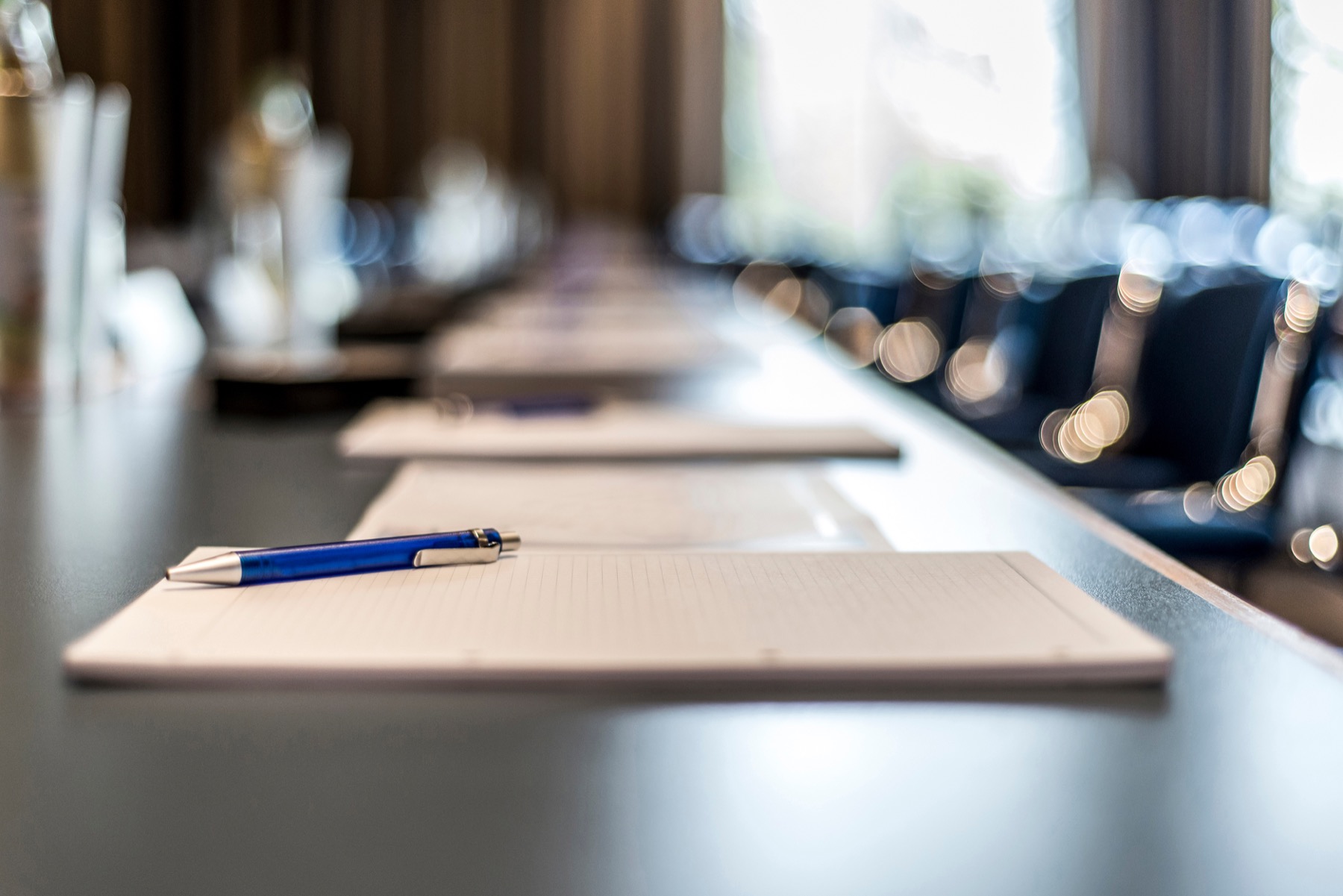 Boardroom table with papers, a pen, and morning light.